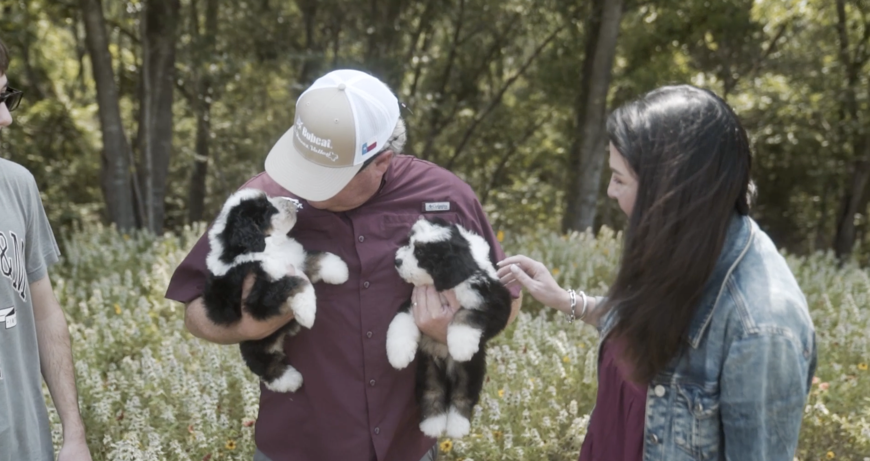lone star pups image of three people, one person is holding two bernedoodle puppies